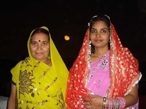 Two Indian women dressed in Indian attire to celebrate Karva Chauth. Full moon is showing in the sky in background.